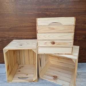 May include: Three wooden crates stacked on top of each other. The crates are made of natural wood and have a rustic look. The crates are empty and have a handle on the front.