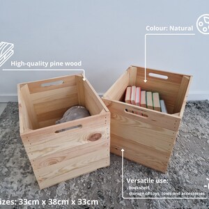 May include: Two natural wood storage crates with handles. The crate on the left is empty and the crate on the right is filled with books. The crates are 33 cm x 38 cm x 33 cm.  The text on the image reads: "High-quality pine wood", "Colour: Natural", "Sizes: 33cm x 38cm x 33cm", "Versatile use: bookshelf, storage of toys, tools and accessories".