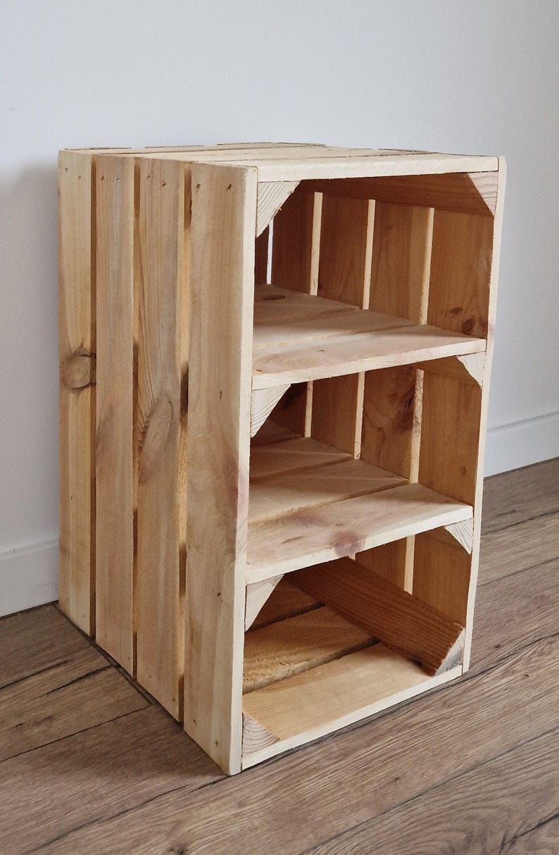 Puede incluir: Una estanter&iacute;a de caja de madera de color marr&oacute;n claro con listones verticales en los laterales y dos estantes interiores horizontales. La estructura est&aacute; hecha de madera de pino natural con vetas visibles y soportes de esquina reforzados.