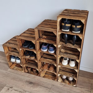 Puede incluir: Un zapatero escalonado construido con cuatro cajas de madera apiladas con un acabado oscuro y quemado. La unidad cuenta con m&uacute;ltiples compartimentos abiertos dispuestos en forma de escalera, que contienen varios estilos de calzado, incluyendo zapatillas y tacones.