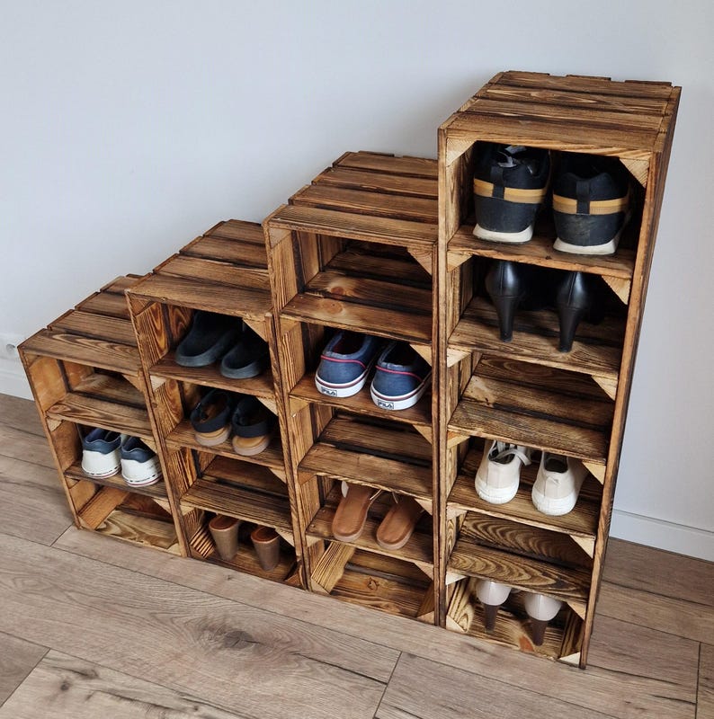 Puede incluir: Un zapatero escalonado construido con cuatro cajas de madera apiladas con un acabado oscuro y quemado. La unidad cuenta con m&uacute;ltiples compartimentos abiertos dispuestos en forma de escalera, que contienen varios estilos de calzado, incluyendo zapatillas y tacones.
