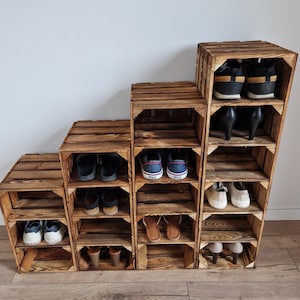 May include: A wooden shoe rack made from repurposed crates. The rack is arranged in a stepped design, with multiple shelves holding various pairs of shoes, including sneakers, sandals, and heels. The wood has a natural, rustic finish.