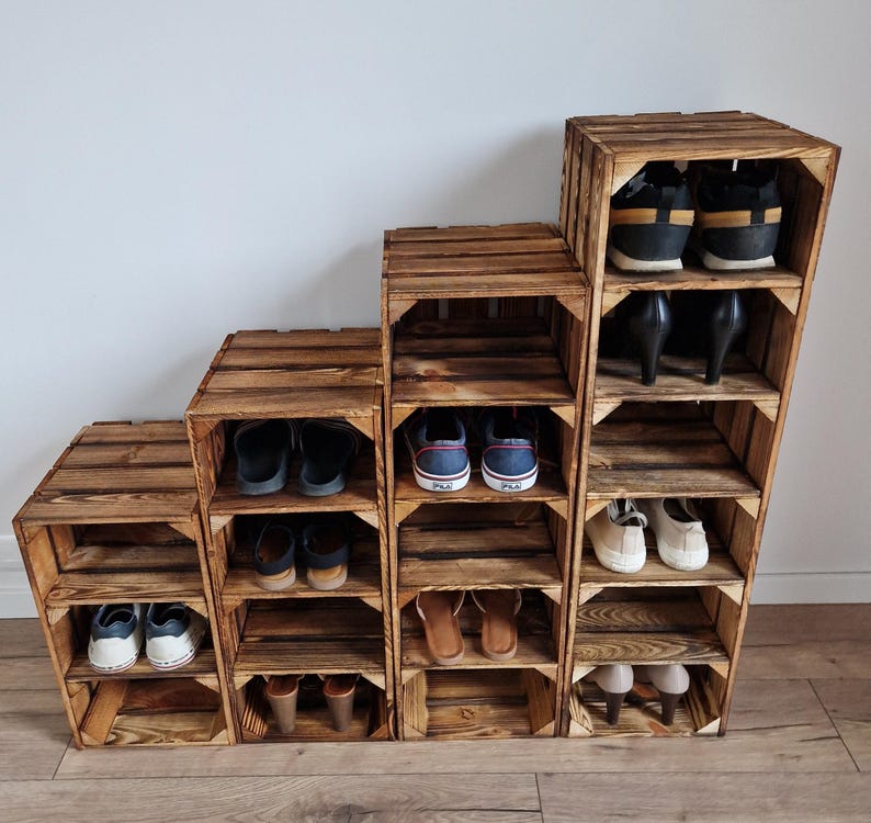 May include: A wooden shoe rack made from repurposed crates. The rack is arranged in a stepped design, with multiple shelves holding various pairs of shoes, including sneakers, sandals, and heels. The wood has a natural, rustic finish.