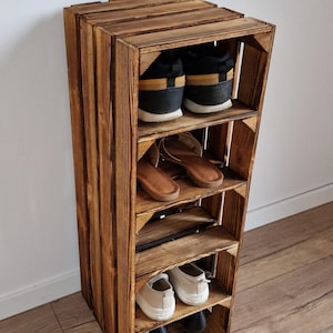Puede incluir: Un zapatero vertical construido a partir de una caja de madera te&ntilde;ida con cuatro estantes horizontales. El estante contiene varios calzados, incluyendo zapatillas negras y amarillas, sandalias marrones, zapatillas beige y tacones negros.