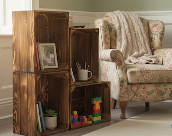 May include: Four stacked, stained wooden crates used as shelving. The crates contain books, a framed photo, a potted plant, pencils, a mug, and colourful wooden blocks. A floral armchair and a rug are in the background.