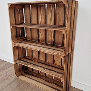 May include: A rustic, wooden shelf unit made from two stacked crates. The shelves are a warm brown color with visible wood grain and dark accents. The unit has three shelves and is designed to lean against a wall.