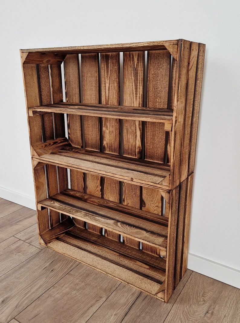 May include: A rustic, wooden shelf unit made from two stacked crates. The shelves are a warm brown color with visible wood grain and dark accents. The unit has three shelves and is designed to lean against a wall.