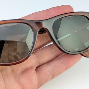 May include: Brown tortoiseshell sunglasses with dark lenses. The sunglasses have a classic, rectangular frame design with a keyhole bridge. The lenses are reflective, and the arms have a slight curve for a comfortable fit.