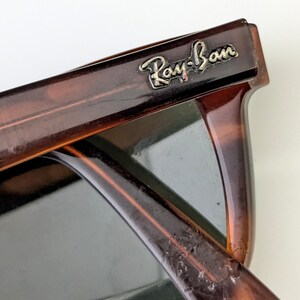 May include: Close-up of Ray-Ban sunglasses with a tortoiseshell frame. The sunglasses have dark lenses and the Ray-Ban logo is visible on the top corner of the frame. The frame is a mix of brown and amber colours.