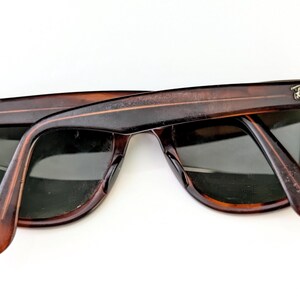May include: Tortoiseshell sunglasses with dark lenses. The Ray-Ban logo is visible on the temples. The sunglasses are set against a white background.