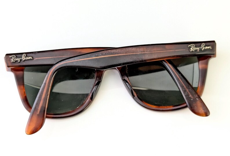 May include: Tortoiseshell sunglasses with dark lenses. The Ray-Ban logo is visible on the temples. The sunglasses are set against a white background.