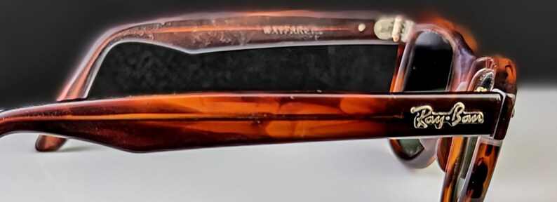 May include: Tortoiseshell sunglasses with the Ray-Ban logo in gold on the temple. The frame features a classic Wayfarer design. The lenses are dark, and the overall style is retro. The text "WAYFARER" is visible on the frame.
