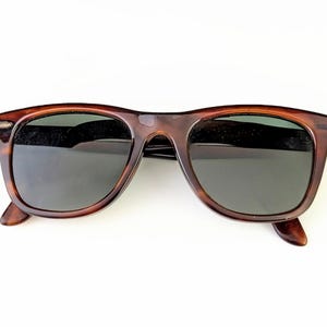 May include: Brown tortoiseshell sunglasses with dark lenses. The classic frame design features a keyhole bridge and a slightly rounded shape. The sunglasses are set against a white background.