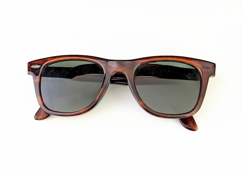 May include: Brown tortoiseshell sunglasses with dark lenses. The classic frame design features a keyhole bridge and a slightly rounded shape. The sunglasses are set against a white background.