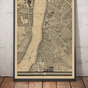 May include: A vintage black and white map of Amsterdam, Netherlands, showing the city's layout and waterways. The map is framed in a black frame and has a decorative border.