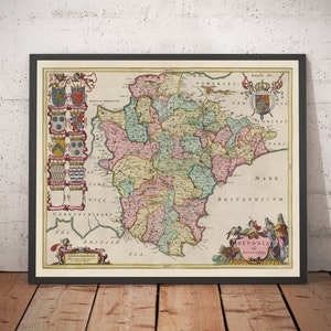 Peut inclure: Carte ancienne encadrée du Devon, en Angleterre, avec des divisions de comté en rose, vert et jaune. La carte comprend des éléments décoratifs tels que des armoiries, des figures et du texte en latin. Le tout est encadré dans un cadre noir.