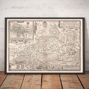 May include: A vintage black and white map of Dorset, England, with the title "Dorsets Hyre" and text describing the area. The map shows the coastline, rivers, and towns. The map is framed in a black frame.