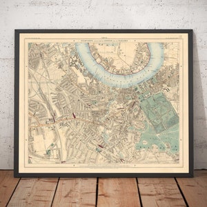 Könnte beinhalten: Eine antike Karte von London und seinen Vorstädten, gedruckt in schwarzer, roter und blauer Tinte auf cremefarbenem Papier. Die Karte zeigt die Themse, die Stadt London und die umliegenden Gebiete. Der Titel der Karte lautet "Stanford's New Pocket Map of London and its Suburbs."