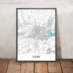 May include: A black and white map of Cork, Ireland, with blue water features. The map is framed in a black frame and is hanging on a white wall.