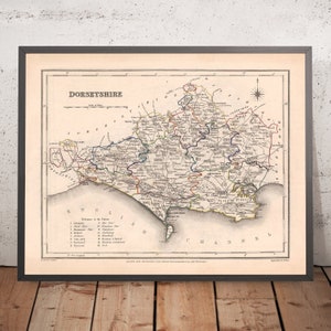 May include: An antique map of the county of Dorsetshire, England, printed in black, red, blue, and green ink on cream paper. The map shows the county's boundaries, towns, and rivers. The title "Dorsetshire" is printed in large, bold letters at the top of the map. The map is framed in a black frame.