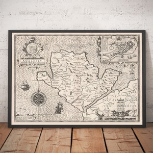Puede incluir: Un mapa vintage en blanco y negro de Anglesey, una isla en Gales, con el título "Anglesey, Antiently called Mona, described and divided into Hundreds". El mapa muestra la costa de la isla, los ríos y las ciudades, con una rosa de los vientos en la esquina inferior izquierda.