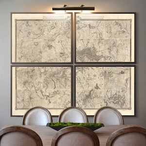 May include: Four framed antique maps in black frames hang on a gray wall above a wooden dining table with six chairs. The maps are in black and white and show a detailed view of a city or region.