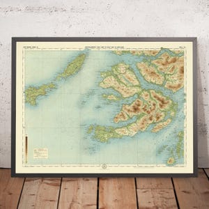 May include: Framed vintage map of Scotland, featuring detailed topographical information. The map displays shades of blue for water, green for land, and brown for elevated terrains. The map is encased in a dark gray frame, resting on a wooden surface.