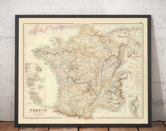 May include: Framed vintage map of France, with detailed geographical features. The map is in a black frame, set against a textured white and grey wall. The map's colours include beige, brown, and pink.