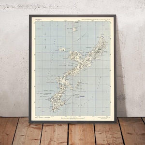 Puede incluir: Un mapa vintage de Okinawa Shima, una isla japonesa, con fondo azul y líneas de cuadrícula. El mapa muestra la costa de la isla, los ríos y las carreteras. El texto "AREA CHART - OKINAWA" está impreso en la parte inferior del mapa.