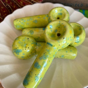 May include: Four green ceramic pipes with blue and yellow speckles. The pipes are arranged in a pile on a white plate.