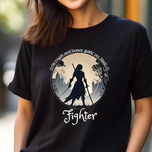 Könnte beinhalten: Schwarzes T-Shirt mit einem Grafikdruck einer Frau in Silhouette, die ein Schwert hält. Die Grafik befindet sich in einem Kreis mit dem Text "Strength and honor guide my blade" und "Fighter" unterhalb des Kreises.