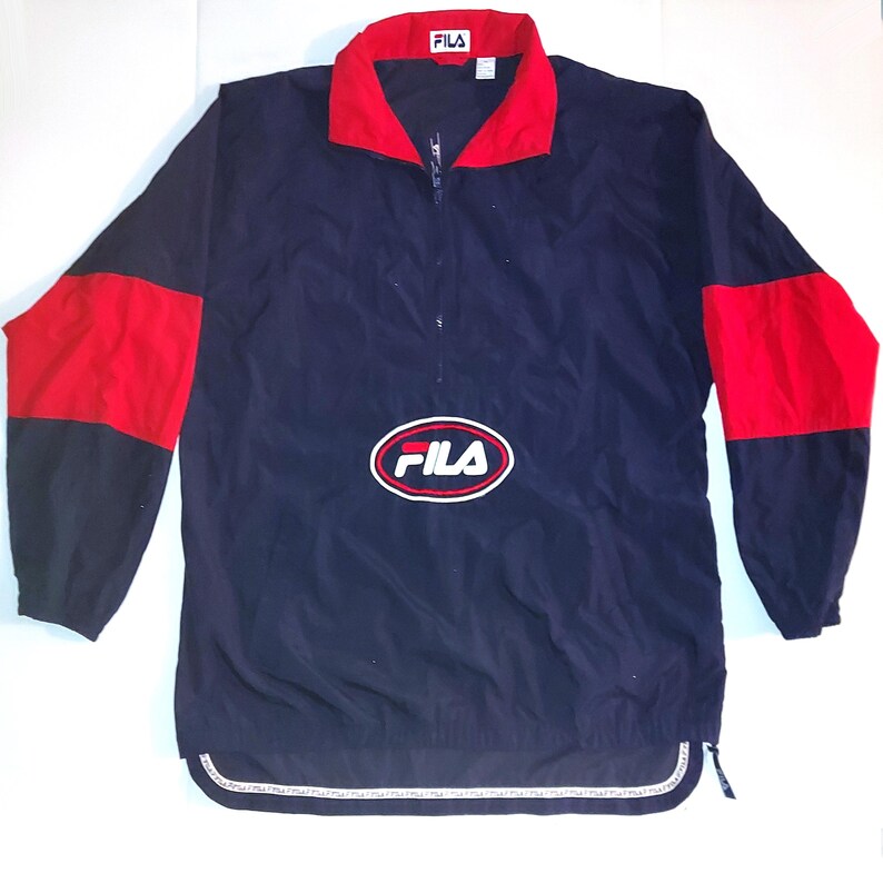 Pu&ograve; includere: Giacca a vento Fila blu navy con dettagli rossi sulle spalle e sul colletto. La giacca presenta una chiusura a mezza zip e il logo Fila sul petto. L'orlo inferiore presenta un motivo a righe bianche e grigie.