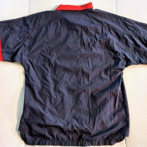 Pu&ograve; includere: Giacca a vento blu navy con colletto e polsini rossi. La giacca ha una vestibilit&agrave; rilassata e un design semplice, adatta per l'abbigliamento casual. Il tessuto sembra leggero e leggermente strutturato.