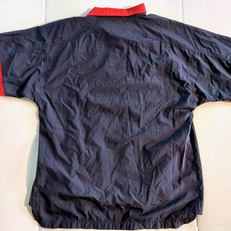 Pu&ograve; includere: Giacca a vento blu navy con colletto e polsini rossi. La giacca ha una vestibilit&agrave; rilassata e un design semplice, adatta per l'abbigliamento casual. Il tessuto sembra leggero e leggermente strutturato.