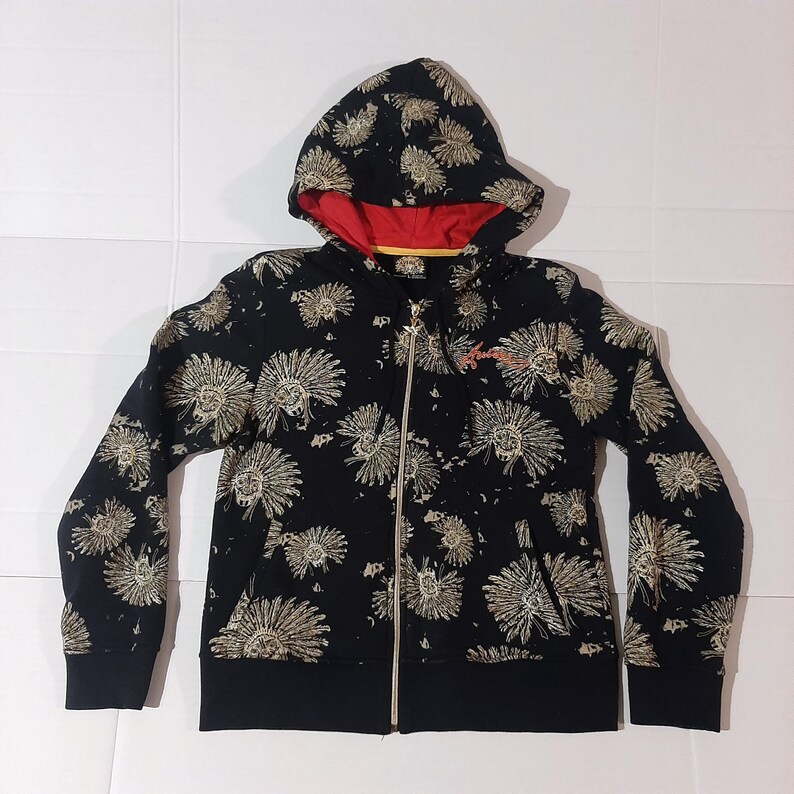 May include: Black zip-up hoodie with a floral pattern. The hoodie features a red lining in the hood and a gold zipper. The floral design is in a light tan color. The cuffs and bottom hem are solid black.