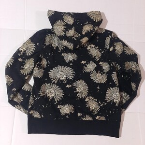 May include: Black hoodie with a repeating pattern of tan Native American headdresses. The hoodie has a black ribbed hem and cuffs, and a lined hood. The design is printed on a black background.