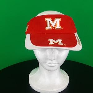 May include: Red and white visor with the letter "M" in white with a gold outline. The visor has a curved brim and is displayed on a white mannequin head. The background is green.