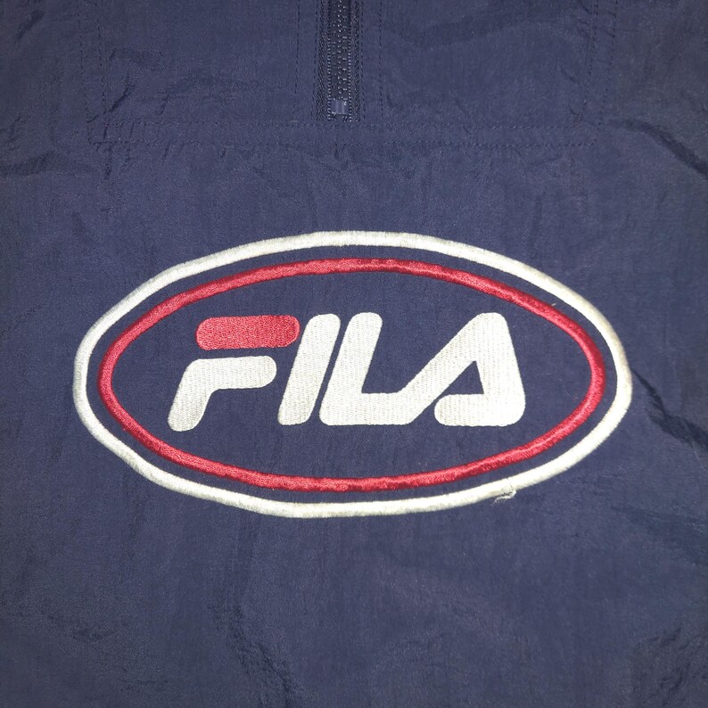 Pu&ograve; includere: Giacca sportiva blu navy con logo FILA. Il logo &egrave; un design ovale con una combinazione di colori rosso e bianco. La giacca ha una chiusura con zip a un quarto sul collo.