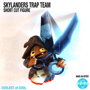 May include: A Skylanders Trap Team Short Cut figure. The figure is brown with yellow eyes and a brown hat. It is holding large blue scissors. The base is red and white. The text "SKYLANDERS TRAP TEAM SHORT CUT FIGURE" is at the top.