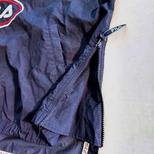 Pu&ograve; includere: Giacca FILA blu navy con logo bianco e rosso in alto a sinistra. La giacca ha una cerniera a tutta lunghezza sul lato e una tasca. Il logo FILA &egrave; visibile anche sulla cerniera.