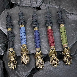 May include: Five lanyards featuring braided cord in black, blue, dark blue, red, and olive green. Each lanyard has a bronze-toned metal charm at the base depicting a bearded face with tentacle-like features, topped with a decorative metal ring.