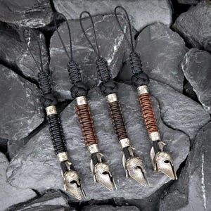 May include: Four black paracord keychains with silver Spartan helmet charms. The keychains are made with different colored paracord, including black, brown, and a lighter brown.