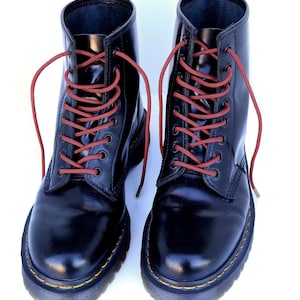 Könnte beinhalten: Schwarze Lederstiefel mit roten Schnürsenkeln. Die Stiefel haben ein gelbes Nähtdetail um die Sohle.