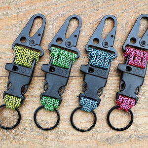 May include: Four black keychains with different colored paracord. Each keychain has a whistle and a metal ring.