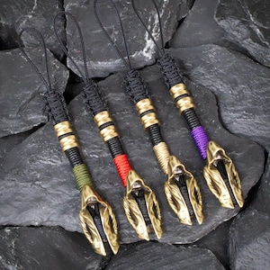 May include: Four ornate keychains with a gold-colored, hooded figure design. Each keychain has a black cord loop and a black and gold-toned handle. The handles are accented with red, green, gold, and purple thread.