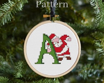 May include: A cross-stitch ornament featuring the letter "A" with Santa Claus peeking out from behind it. The letter is green and Santa is wearing a red suit with white trim.