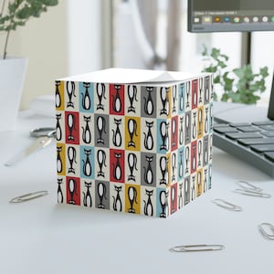 May include: A square notepad with a repeating pattern of black cats on a white background. The cats are outlined in red, yellow, blue, and gray.