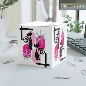 May include: White square box with a pink, black and grey geometric design featuring stylised cats. The design includes a black cat with a curled tail and a pink flower.