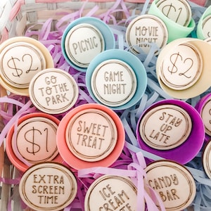 May include: A collection of wooden tokens in plastic Easter eggs. The tokens feature various activities and amounts of money, such as "Game Night", "Sweet Treat", "$2", "$1", "Go to the Park", "Movie Night", "Stay Up Late", "Picnic", "Extra Screen Time", "Ice Cream", and "Candy Bar".