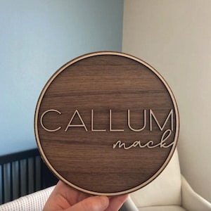 Op de afbeelding: Een rond houten bord met een lichtbruine houtnerf. Het bord heeft een witte rand en de naam "CALLUM mack" is gegraveerd in witte letters.